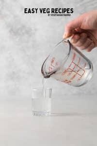 a glass measuring cup pouring a drink into a shot glass.