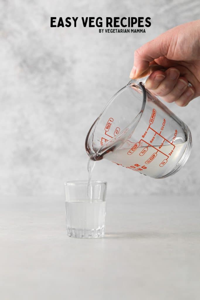 a glass measuring cup pouring a drink into a shot glass.
