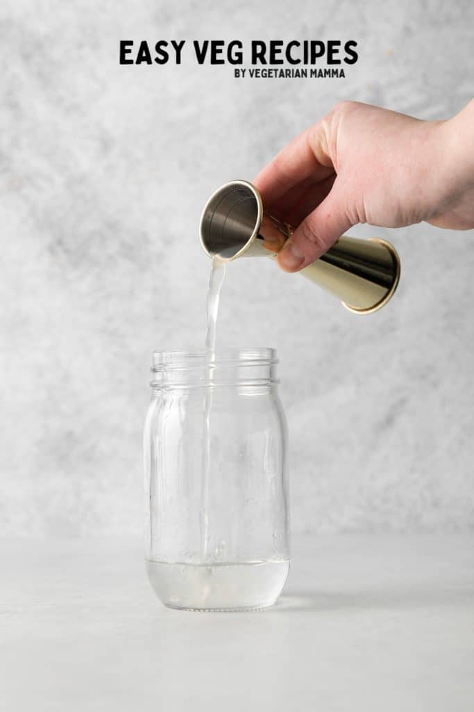 sweet and sour mix being poured into a jar with a metal jigger.