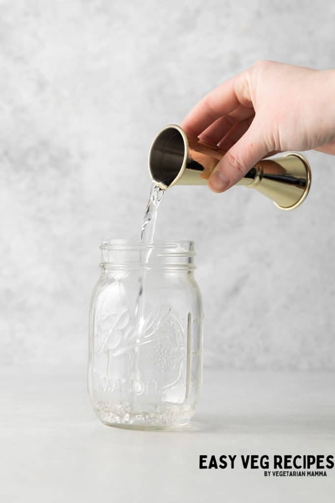 Vodka poured from a jigger into a ball jar.
