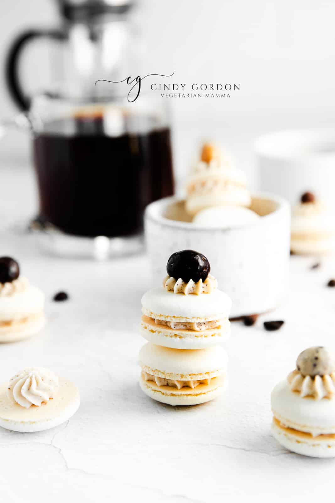 a stack of coffee macarons in front of a fresh press of coffee. 