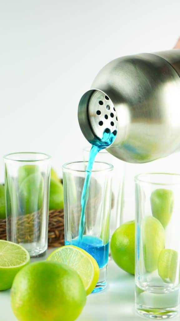 blue kamikaze shot poured from a metal shaker into tall shot glasses.
