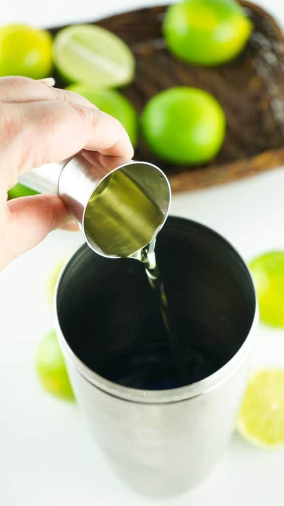 alcohol poured into a shaker. Limes are in the background