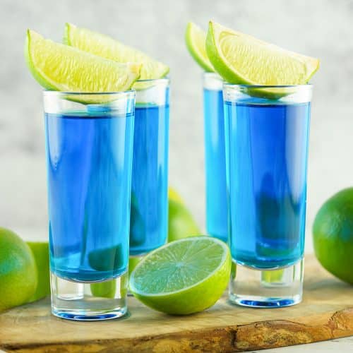 four blue kamikaze shots with lime wedges on top.