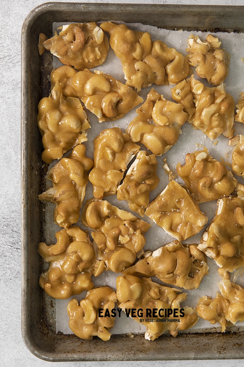 cashew brittle broken up into pieces on a parchment lined baking sheet