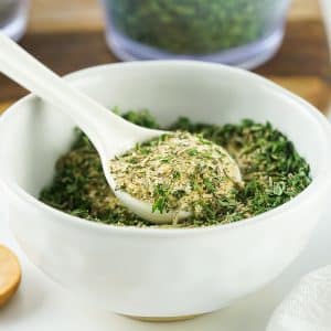 a white bowl of spaghetti seasoning with a small white spoon.