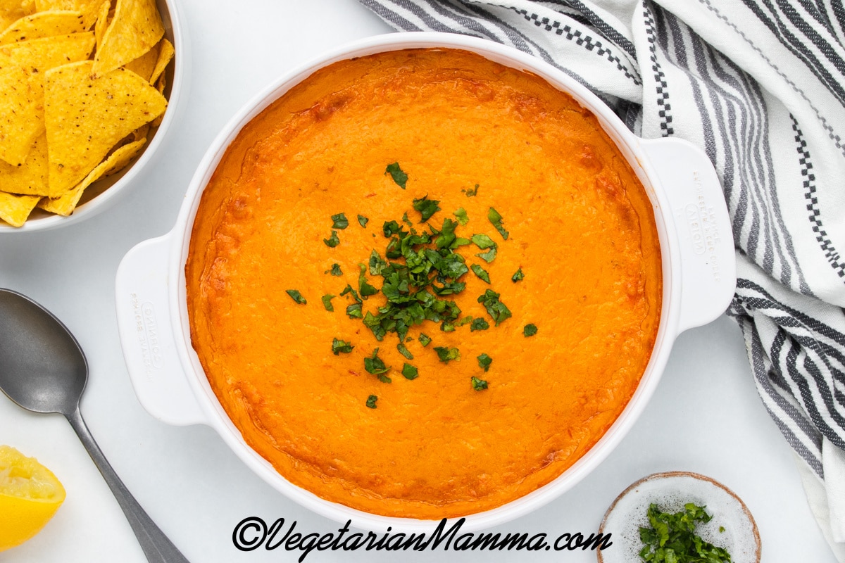 a spoon has mixed up a dish of hot vegan buffalo chicken dip.