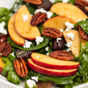closeup of a salad of greens topped with apples, grapes, pecans and feta