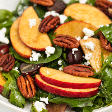 closeup of a salad of greens topped with apples, grapes, pecans and feta