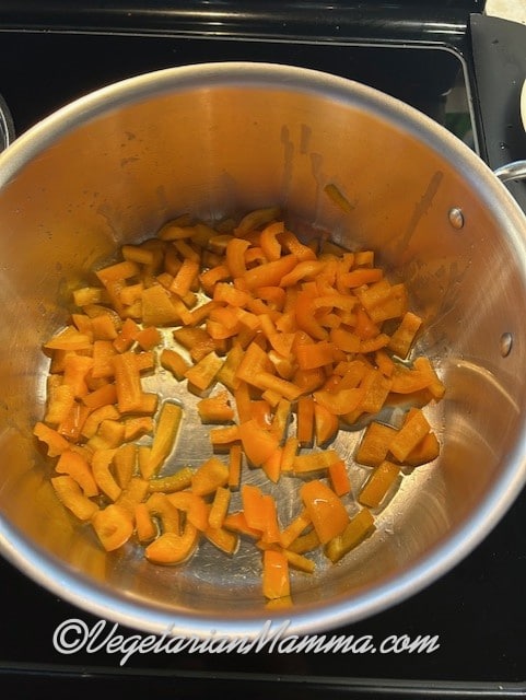In a large stockpot, orange bell peppers are sautéing.