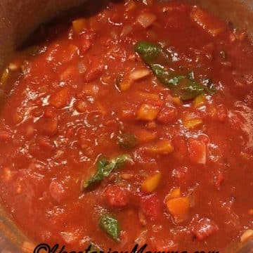A stock pot filled with sauces, including fresh basil and oregano.