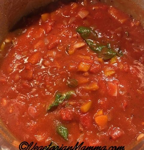 A stock pot filled with sauces, including fresh basil and oregano.