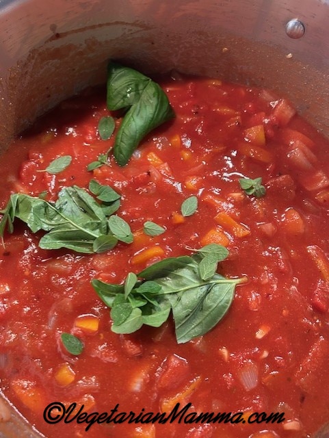 A large stock pot with tomato sauce with fresh basil, and oregano.