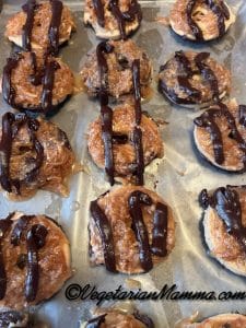 Each cookie drizzled with chocolate sauce after topped with caramel coconut and dipped in chocolate.