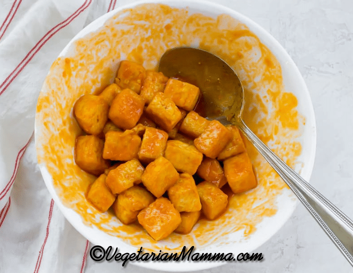 Buffalo sauce tossed with tofu in a bowl.