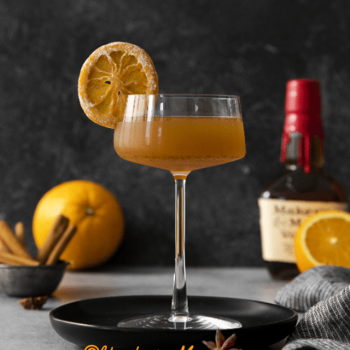 Winter Orange Whiskey Cocktail in a stem glass with a dried orange for garnish on a black coaster.