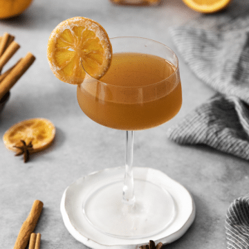 Winter Orange Whiskey Cocktail in a stem glass with a dried orange for garnish on a white coaster.