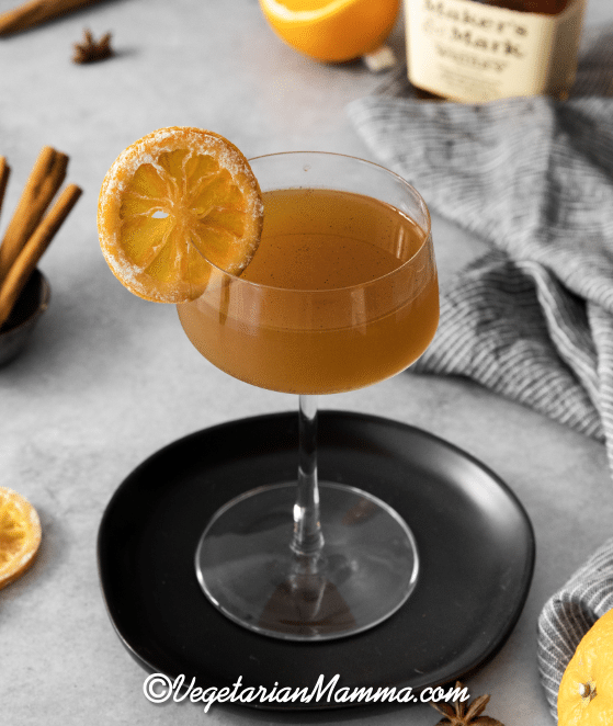 Winter Orange Whiskey Cocktail in a stem glass with a dried orange for garnish on a black coaster.