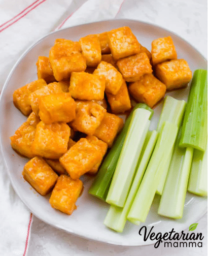 A white plate full of buffalo tofu bites and celery.
