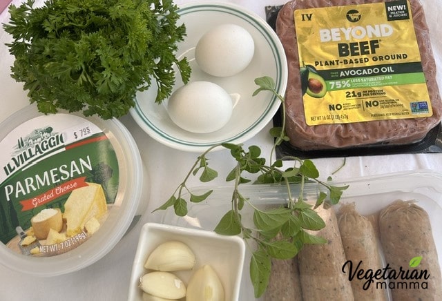 A group of ingredients for Impossible Italian Meatballs, including Impossible Beef, Impossible Sausage, garlic cloves, eggs, Parmesan cheese, parsley, and oregano.