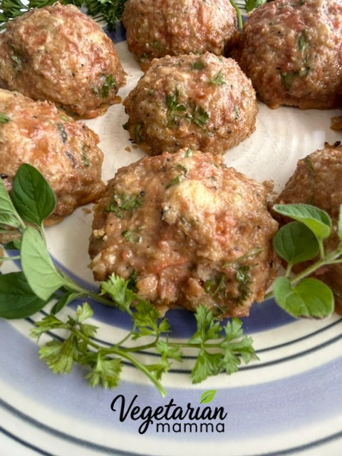 A plate of Impossible Italian meatballs with a few sprigs of parsley and oregano 