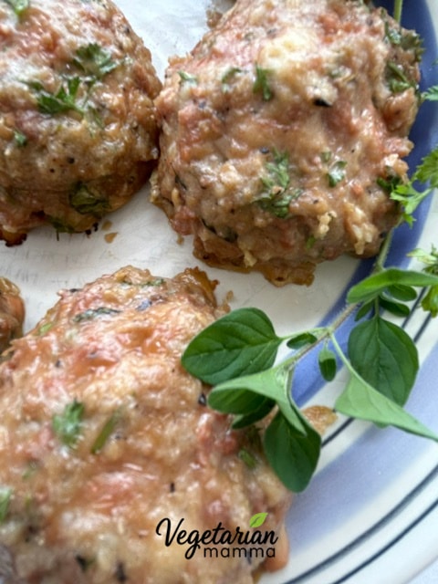 A few Impossible Italian Meatballs on a plate with a sprig of oregano. 