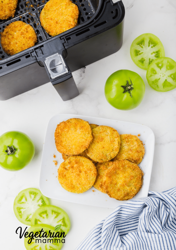 An air fryer basket, a couple of green tomatoes, and completed fried green tomatoes fresh from the air fryer.